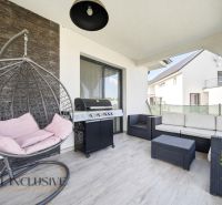 A terrace of a family house with comfortable rattan seating and a grill on a floor with a wooden decor.