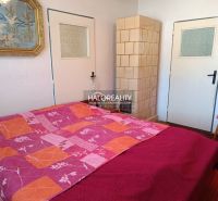 A bedroom in a family house with a tiled stove, a painting, and a chair.