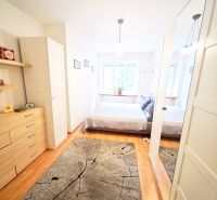 A bright bedroom in a two-room apartment with wood-patterned flooring and a mirrored wardrobe.