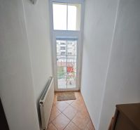 A narrow hallway with a window and a radiator in a 2-room apartment, tiles on the floor.