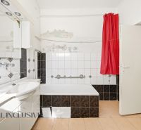 A bathroom in a family house with a bathtub, white tiles, and a red curtain.