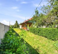A family house in Hviezdoslavov with a garden, green shrubs, and a grassy plot by a concrete fence.