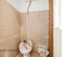 A simple bathroom with a toilet tiled in beige tiles in a family house.