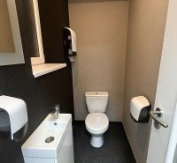 A toilet with a sink and a paper dispenser in offices.