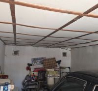 A garage with a white fan, stored items, and a parked car.