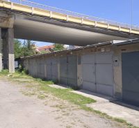 Garages on Jesenského Street in Zvolen under the bridge, surrounded by greenery and a gravel road.