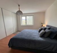 Bedroom in a family house with a bed, wooden decor flooring, and a built-in wardrobe.