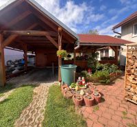 A family house in Bacúch with a shelter, a garden, and stored wood, sunny day.
