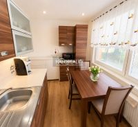 A kitchen in a studio apartment with wooden decor, a dining table, and a sunny window.