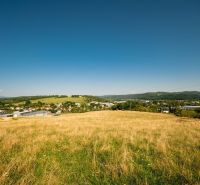 A landscape with a grassy meadow and a village in the background in the Banská Bystrica district, Banskobystrický region, suitable for residential plots.