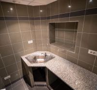 A small kitchen with gray tiles, a granite countertop, and a stainless steel sink.