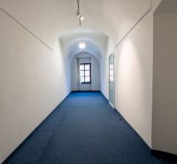A narrow corridor with a curved ceiling, carpet, and a large window at the end.