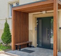 Entrance to an apartment building in Poprad with a wooden shelter and a bench.