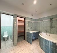 A bathroom in a family house with a bathtub, green tiles, and access to a toilet.