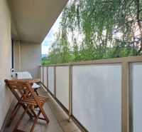 The balcony of a 2-room apartment with folding chairs and a table, view of greenery.