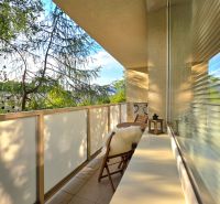 A balcony of a 2-room apartment with a view of greenery and comfortable seating.