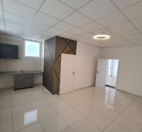 An office space with a kitchenette and a light floor with a wall decoration.