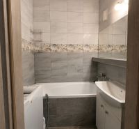 A bathroom in a 3-room apartment with gray tiles, a bathtub, and a washing machine.