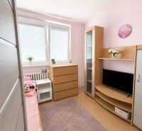 Children's room with wood-patterned flooring, pink walls, and wooden furniture in a three-room apartment.