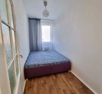 A simple bedroom with a bed, neutral walls, and a wooden decor floor in a 2-room apartment.