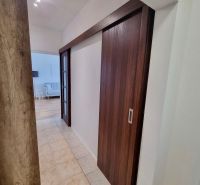 A hallway with sliding doors, tiles, and a view into the living room in a 2-room apartment.