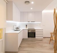 A kitchen in a holiday apartment with white cabinets and wood-patterned flooring.