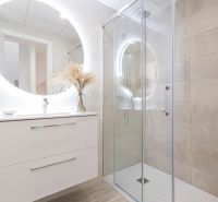 Bathroom in a holiday apartment with a large illuminated mirror and a shower stall.