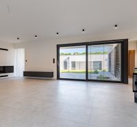 A spacious living room with a fireplace, large windows, and light flooring in a family house.