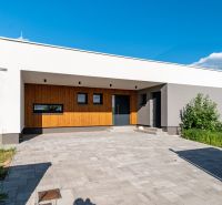 A family house in Košice-okolie with a minimalist facade, wooden elements, and a paved area.