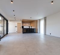 A minimalist interior of a family house with a kitchen, large windows, and light flooring.