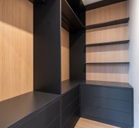 Corner built-in wardrobe with black drawers and wooden shelves in a family house.