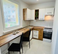 A kitchen in a studio apartment with white cabinets and a wood-patterned floor.