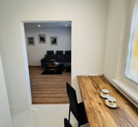 Interior of a 1-room apartment with a wooden decor floor, a sofa, and a table by the window.