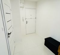 A white entrance hall with tiles and a dark bench in a studio apartment.