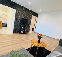 Living room of a one-room apartment with a wooden floor and flowers on the table.