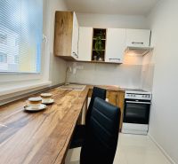 A kitchen in a studio apartment with wood-patterned flooring, white cabinets, and appliances.