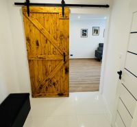 Interior with sliding wooden doors leading to a studio apartment with wood-patterned flooring.