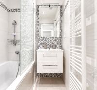 A bathroom in a 2-room apartment with a bathtub, a mirror, and tiles with a mosaic design.
