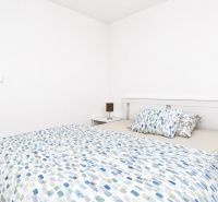 Bedroom in a 2-room apartment with a bed and wooden floor, white wall, nightstands.