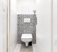 A toilet with mosaic tiles in a 2-room apartment, floor with wood decor.