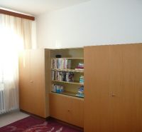 A room in a 2-room apartment with a bookshelf and a large wardrobe, floor with wooden decor.