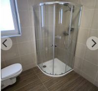 Bathroom in a studio apartment with a corner shower and a wooden decor floor.
