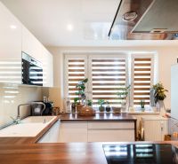 A kitchen in a 3-room apartment with plants on the windowsill and a floor with a wooden decor.