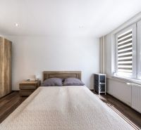 A bedroom with a bed, wood-patterned flooring, and large windows in a three-room apartment.