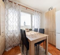 A dining table with four chairs in a three-room apartment, curtains with a geometric pattern.