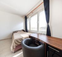 A room in a three-room apartment with a bed, a table, and windows with dark curtains.