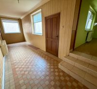 A hallway in a family house with tiles, light-colored walls, and a window with blinds.