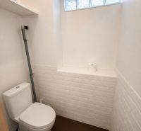 A toilet with white tiles and a roll of toilet paper in a family house.