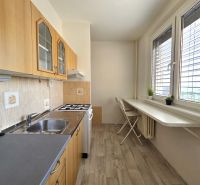 A kitchen in a one-room apartment with a wooden decor floor and white furniture.