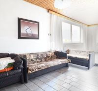 A room in a family house with a sofa, a painting on the wall, and large windows.